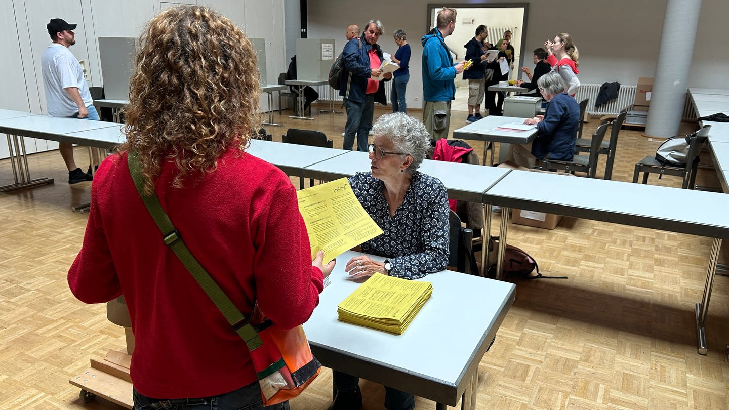 Frau steht mit Wahlunterlagen vor der Wahlurne