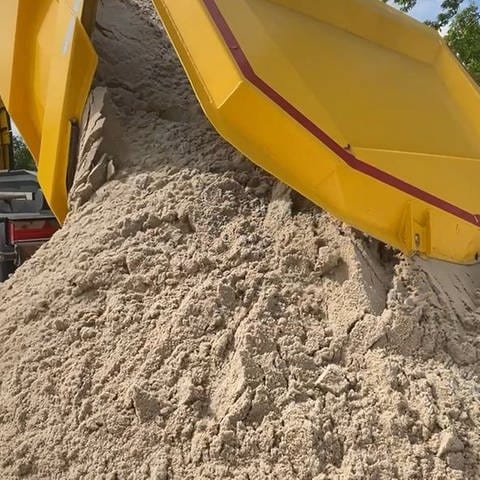 Ein Laster kippt eine ganze Ladung Sand auf den Boden.