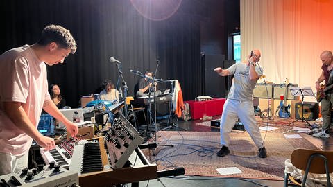 Zanger Thomas D van Die Fantastischen Vier staat op het podium, met Mark Ulrich op de voorgrond keyboard.