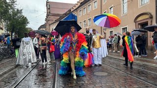 Mehrere Menschen in Regenbogenfarben gekleidet und mit Regenbogen-Schirmen.
