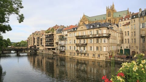 Neben einem Fluss erstreckt sich die Altstadt von Metz. Darüber hinaus ragt die Kathedrale.