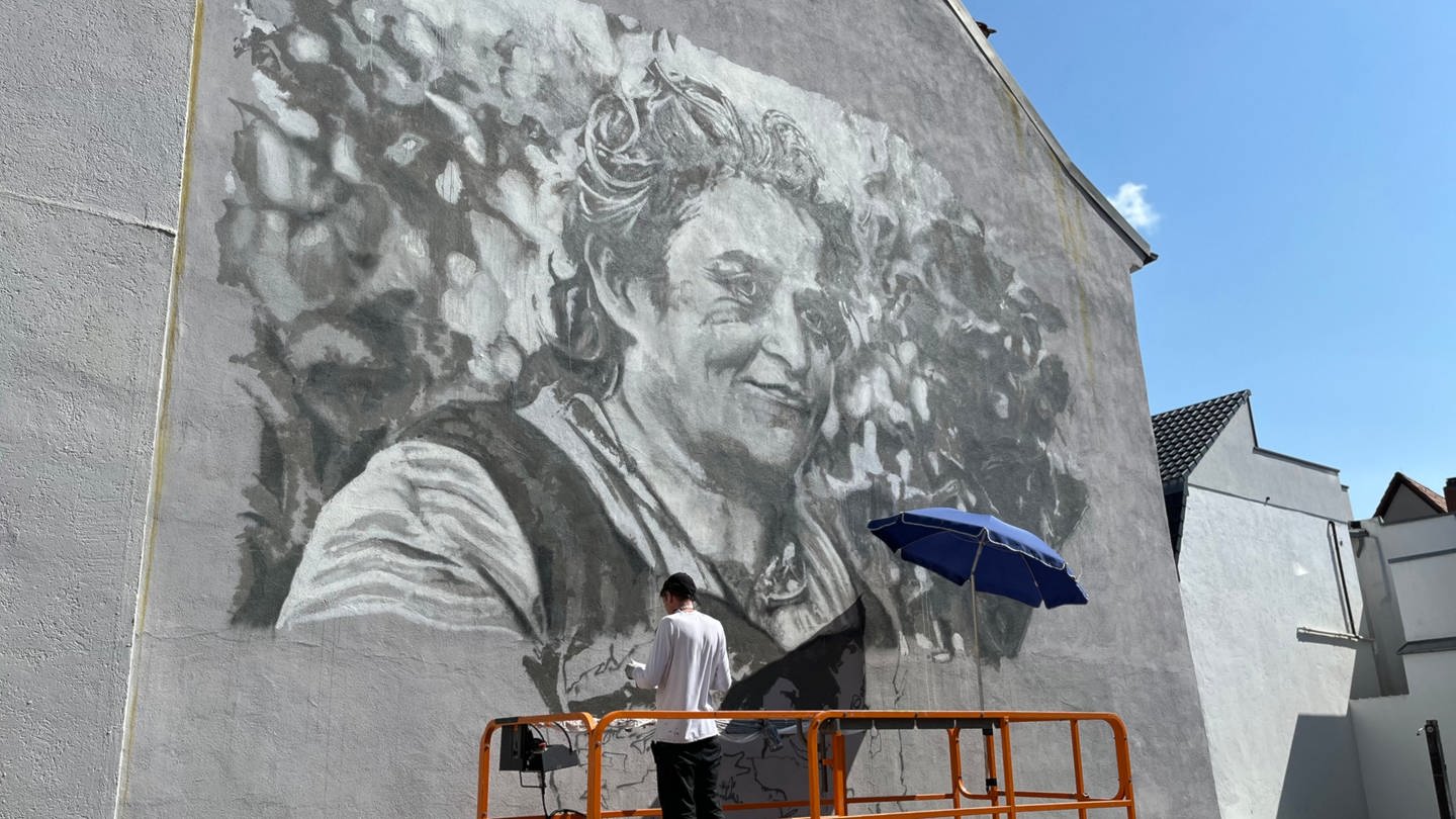Ein Mural-Künstler malt ein schwarz-weiß Porträt von Marie Geck an eine Hauswand in Offenburg.