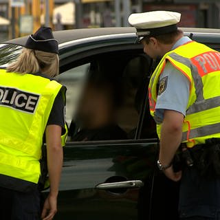 Eine französische Polizistin und ein deutscher Polizist kontrollieren gemeinsam den Fahrer eines schwarzen Autos.