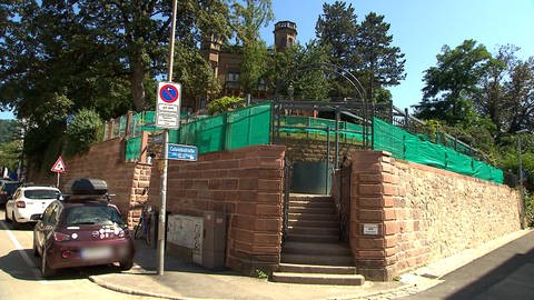 Eine Treppe führt auf eine Terrasse, die von grünen Sonnenschutztüchern bedeckt ist. 