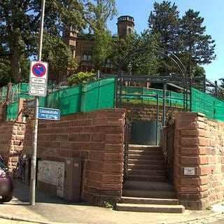 Eine Treppe führt auf eine Terrasse, die von grünen Sonnenschutztüchern bedeckt ist. 