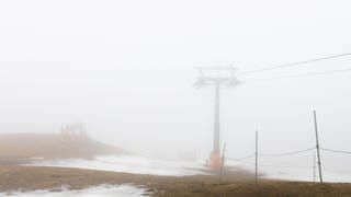 Schneereste liegen neben einem Masten der stillstehenden Feldbergbahn auf dem Gipfel des Feldberg.