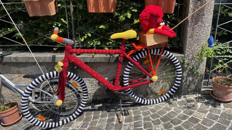 Ein in roter und gelber Wolle umhülltes Fahrrad steht auf dem Bürgersteig.