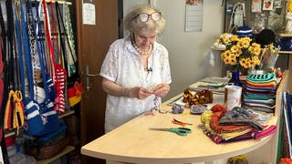 Gisela Mahler häkelt an der Ladentheke, im Hintergrund sind verschiedene Produkte ihrer Strick-Boutique in Bonndorf.