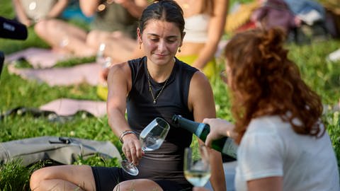 Eine Teilnehmerinn schenkt einer anderen Wein ein. Während der Yoga - Übungen im Weinberg wird Wein ausgeschenkt. 