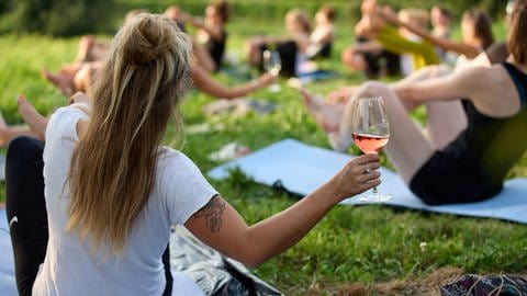 Eine Frau hält während einer Yoga-Stunde ein Weinglas in der Hand.