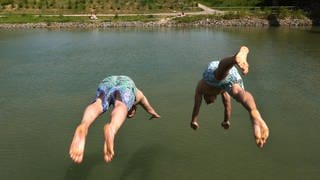 Zwei junge Männer springen in einen Fluss.