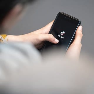 Eine Jugendliche schaut auf ein Smartphone mit angezeigtem TikTok-Logo