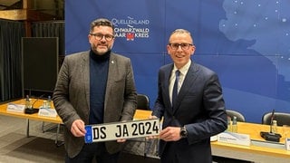 Niko Reith (FDP) und Landrat Sven Hinterseh (CDU) nach der Abstimmung für die Wiederkehr des Donaueschinger Altkennzeichens "DS". Mit einem Ansichtsexemplar eines Autokennzeichens. 