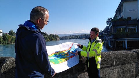 Die Projektverantwortlichen Manuel Schöb (links) und Jochen Ulrich zeigen auf einer Karte, wo der Rhein vertieft werden soll.