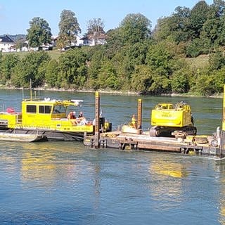 Auf einem Ponton auf dem Wasser heben gelbe Maschinen akutell probeweise ein Stück des Rhein-Flussbetts aus.