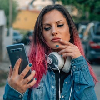 Eine junge Frau schaut zweifeld auf ihr Smartphone. 