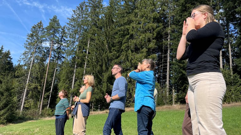 Teilnehmer einer Jodel-Wanderung stehen am Waldrand und jodeln