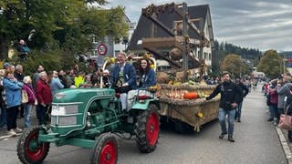 Zwei Teilnehmer des Erntedankfestumzugs in Brigachtal sitzen auf einem Traktor, der einen großen Festwagen zieht.