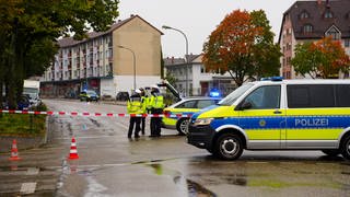 Auf einer Straße stehen mehrere blaue Polizeiwagen und Polizisten in Uniform.