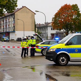 Auf einer Straße stehen mehrere blaue Polizeiwagen und Polizisten in Uniform.