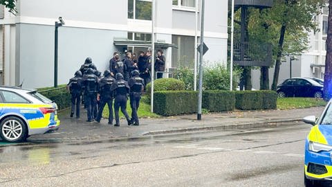 Auf einer Straße stehen mehrere blaue Polizeiwagen und Polizisten in Uniform.