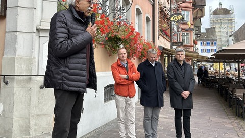 Älterer Mann mit Brille steht in Waldshut vor einem großen Gebäude und spricht in ein Mikrofon.