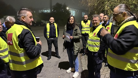 Menschen in gelben Westen, mit dem Logo von verd.i, stehen auf einem Parkplatz.