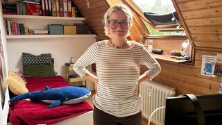 Junge Frau steht in ihrem Mini-WG-Zimmer, das sogar noch Dachschräge hat.