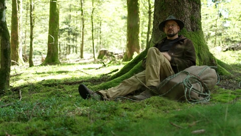 Ralf Greiner lehnt sich an einem Baum an, sein Rucksack liegt neben ihm. 