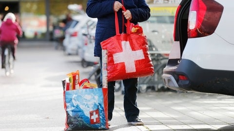 Ein Einkaufstourist stellt seine Schnäppchen in Einkaufstüten mit schweizer Flagge darauf ins Auto.