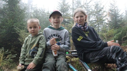 Lenni, Linus und Leya sitzen auf einem Holzstamm. Sie dürfen nach harter Arbeit auch eine Pause genießen.