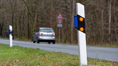 Ein Auto fährt an einem Leitpfosten vorbei, die mit blauen Wildwarnreflektor bestückt worden sind.