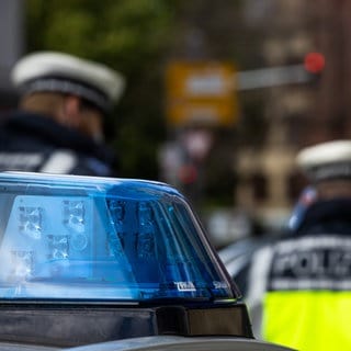 Zwei Polizeibeamte stehen zwischen zwei Einsatzfahrzeugen der Polizei