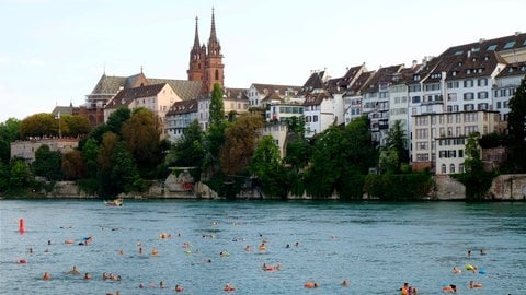 Mehrere Personen nehmen am Basler Rheinschwimmen vor der Altstadtkulisse teil.