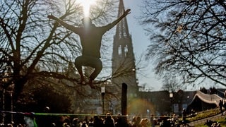 Ein Mann springt vor dem Freiburger Münster im Stadtgarten auf einer Slackline. 