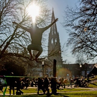 Ein Mann springt vor dem Freiburger Münster im Stadtgarten auf einer Slackline. 