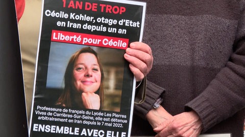 Plakate fordern die freilassung von Cécile Kohler. Neben weißem Text auf schwarzen Grund ist ihr Foto zu sehen.