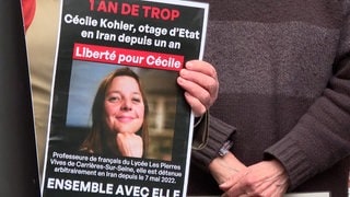 Plakate fordern die freilassung von Cécile Kohler. Neben weißem Text auf schwarzen Grund ist ihr Foto zu sehen.