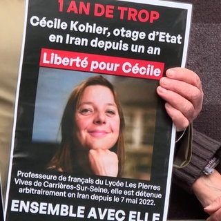 Plakate fordern die freilassung von Cécile Kohler. Neben weißem Text auf schwarzen Grund ist ihr Foto zu sehen.