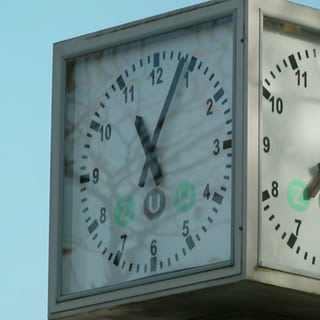 Eine quadratische weiße öffentliche Uhr an einer Freiburger Haltestelle.