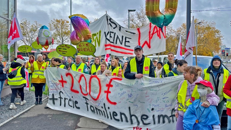 Die Streikenden tragen Transparente, Schilder und auch bunte Luftballons. 