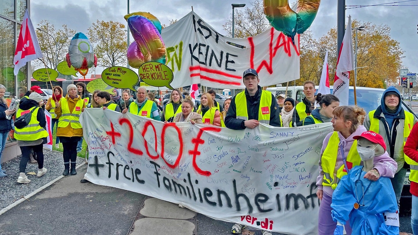 Menschen mit Warnwesten stehen an Ständen der Gewerkschaft Verdi vor einem Gebäude der Uniklinik.