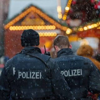 Zwei Polizisten stehen auf dem Weihnachtsmarkt in Frankfurt am Main. Man sieht ihren Rücken, die beiden Sprechen miteinander.