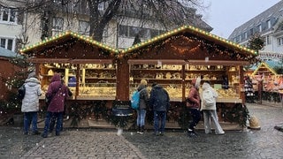 Pünktlich zur Eröffnung des Weihnachtsmarktes fällt auch in Freiburg der erste Schnee. Menschen bestaunen die Stände auf dem Rathausplatz.