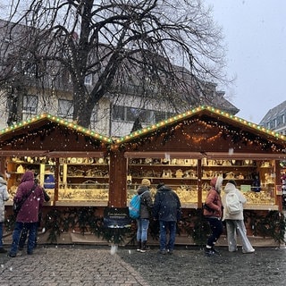 Pünktlich zur Eröffnung des Weihnachtsmarktes fällt auch in Freiburg der erste Schnee. Menschen bestaunen die Stände auf dem Rathausplatz.