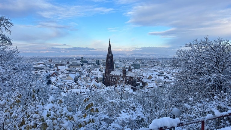 Freiburg von oben: viele verschneite Dächer, in der Mitte das Freiburger Münster. 