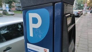 Parkautomat, im Hintergrund parkende Autos