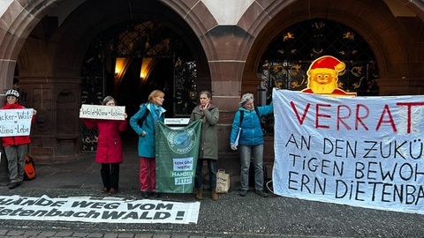 Vor dem Rathaus stehen mehrere Menschen und halten Schilder und große Plakate hoch.