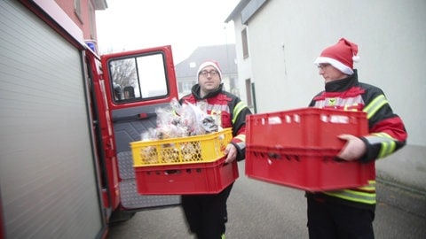 Zwei Männer in Feuerwehrkleidung mit Tüten voller Plätzchen  - die Feuerwehr Norsingen liefert selbstgebackene Plätzchen aus