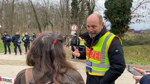 Ein Polizeisprecher im Gespräch mit einer Frau an einer Absperrung vor dem besetzten Waldstück